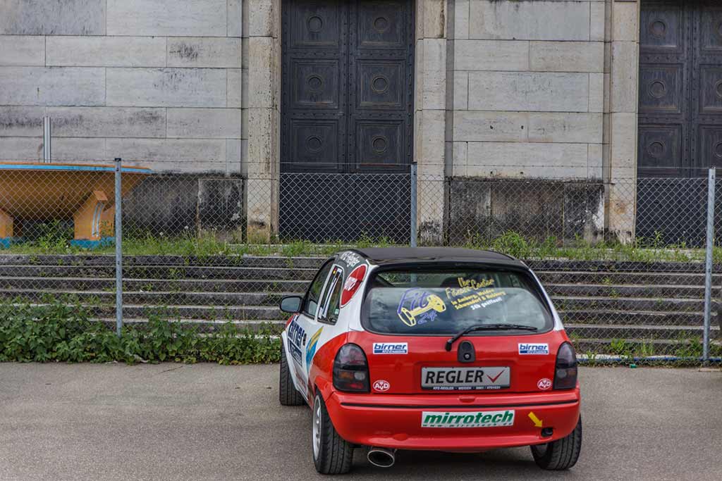 rot weißer Opel Corsa Rennwagen vor Mauer Rückseite Steintribüne